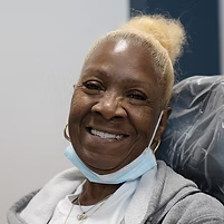 patient_woman01c Smiling patient in dental chair with mask pulled down, appearing pleased after treatment.