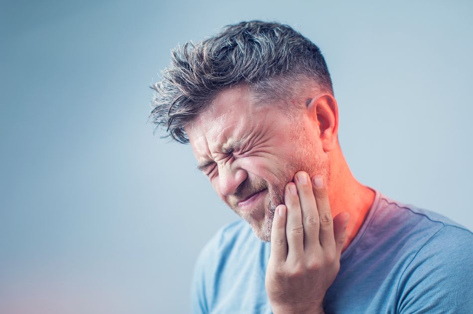 A middle-aged man grabbing at jaw with hand, clearly experiencing a toothache
